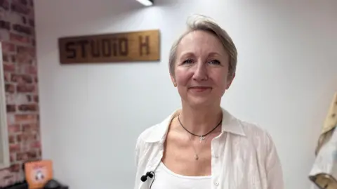 A woman stood in a barbershop with the sign "studio H" visible behind her.