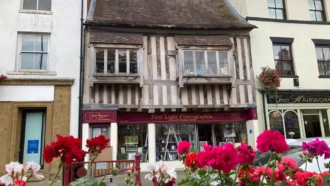 Martin Heath/BBC Timber-framed two-storey building with shop window on ground floor and flowers in the foreground