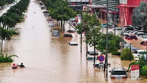 Getty Images Vehicles inundated while two people hold on to each other as they wade through floodwaters in the city of Nha Trang 