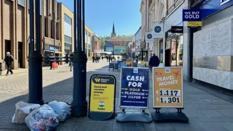 BBC Walsall shopping street, showing rubbish bags and shop boards, with one shop boarded up