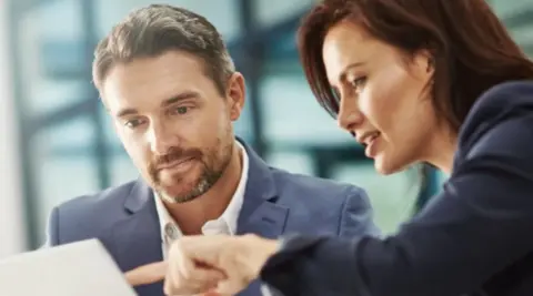 A man and woman both dressed in business attire look at a computer screen