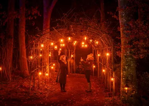 Phil Wilkinson Two people take a picture underneath a tunnel of hanging lights