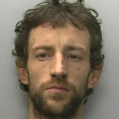 Devon and Cornwall Police A mug shot of Jean-Luc Coombe with short curly brown hair and a beard.