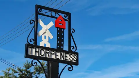 Getty Images Metal village sign that says "Thorpeness", made from metal and featuring representations of a windmill and The House in the Clouds, a water tower disguised as a house.