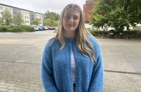 Student Holly standing in the University of Gloucestershire campus wearing a bright blue cardigan