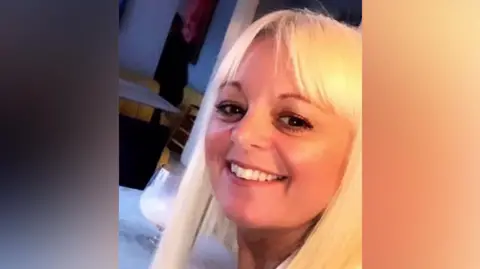 Consortium of Lancashire and Cumbria Local Medical Committees Faye Tomlinson smiling. It is a close up, she has blonde hair and a fringe. In the background there is a table with a glass on it.