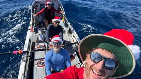 Handout Four people smiling on a small boat. They are wearing Santa hats.