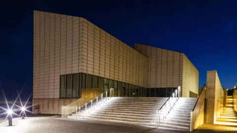 Getty Images A modern gallery is lit up a night. 