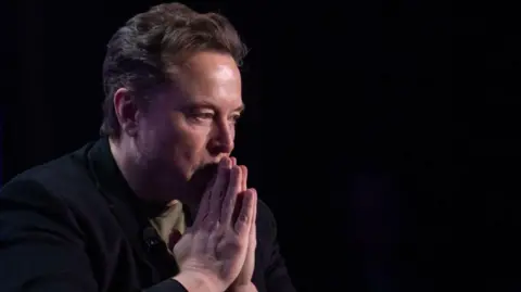 Elon Musk holds his hands as if in prayer