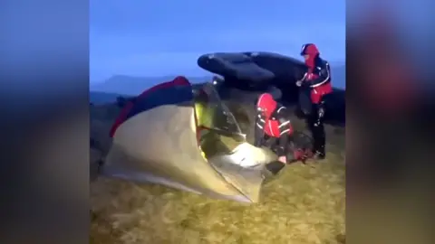 One rescuer kneels outside a tent while another stands.