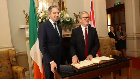 Government Information Service/Shutterstock Simon Harris stands beside Sir Keir Starmer as the UK prime minister signs the visitors' book in Farmleigh House, Dublin