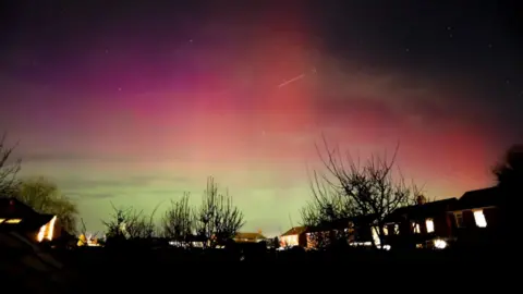 Northern Lights display seen over Broughton in North Lincolnshire. There are silhouetted trees and houses in the picture.