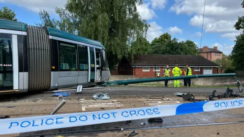 Crashed tram, damaged lamp-post and people in hi-vis jackets