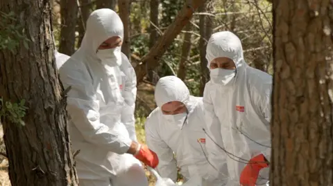 BBC Four people in personal protective clothing carry a body bag through a forest and up a hill 