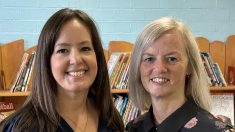 Two women stood in front of a bookcase filled with children's books