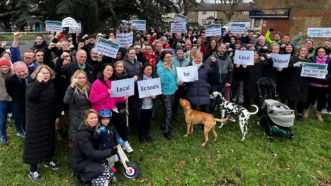 Campaigners, including parents, children and a couple of dogs, pictured protesting against potential admissions changes being made by Hinchley Wood School. A number of parents are holding up signs spelling out 'Local Schools for Local Children'. 