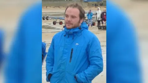 Sam wearing a blue coat on a beach