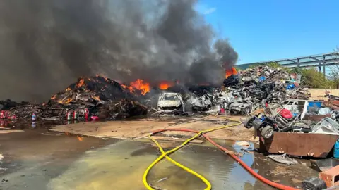 Nottinghamshire Fire and Rescue Service Hoses on the floor in front of a heap of burning scrap