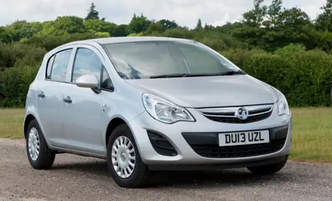 Getty Images A 2013-registered small silver car parked on a gravel path with grass and bushes in the background. 