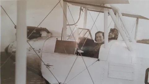 Catherine Beale Flight Captain Susan Slade next to a co-pilot in an open cockpit of an aeroplane.