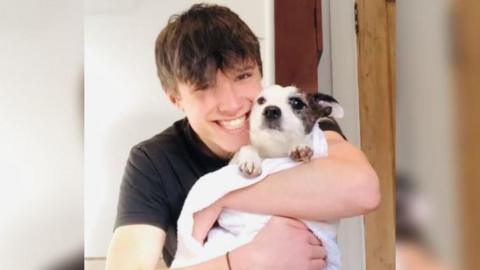 Barney smiling in black top holding a dog 