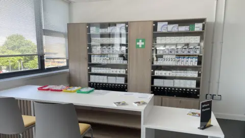 A large cabinet in a classroom has medicines behind glass doors.