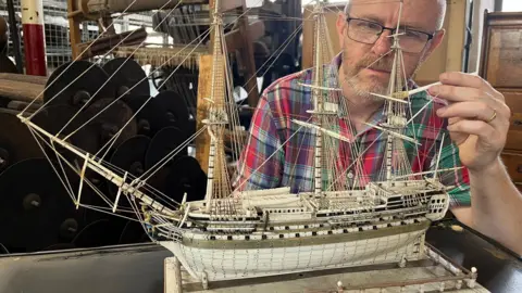 Leeds Industrial Museum A man cleans a model ship made of ivory using a tiny paint brush