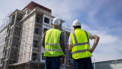 Getty Images two builders look up at a construction site which appears to be blocks of high rise flats