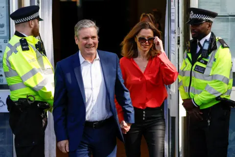 PA Media A 2022 image of Sir Keir Starmer and his wife Victoria leaving a polling station. Two police officers stand on either side of the doors. 