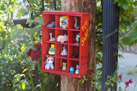 Rachael Harms Mahlandt A toy swap box painted in red, with little toys in each section