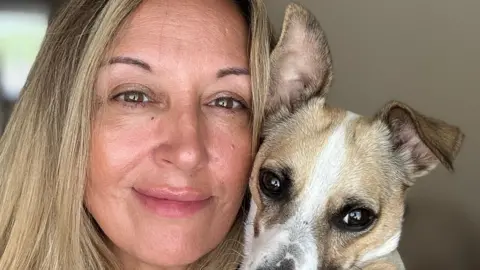 Lisa Kay Lisa Kay, a woman with long blonde hair, smiles into the camera, holding her pet dog up to it as well.