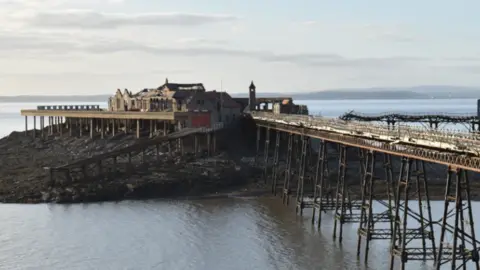 Looking across to Birnbeck Pier from the shore on an overcast day. The pier is dilapidated and looks neglected