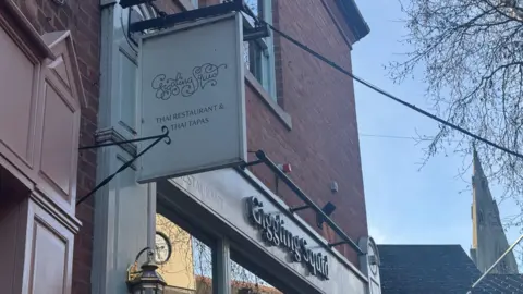 The signage above the restaurant with the cathedral spire in the background