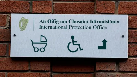 Reuters The exterior sign of the International Protection Office in Dublin. The sign shows a icon of a pram, a wheelchair user and an arrow pointed up.