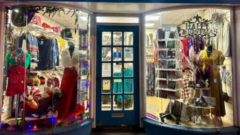Claire House The shop front of Claire House with bowed windows and Christmas displays including ornaments, party dresses and Christmas jumpers.