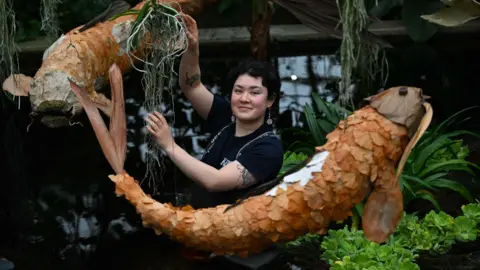 Getty Images One of Kew's horticulturalists stands in a dark pond with orange koi fish sculptures floating above them