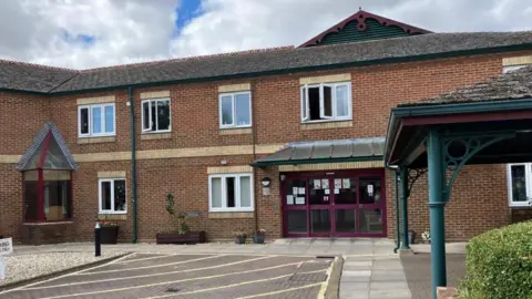 Two story red brick assisted living complex, with a maroon-panelled glass fronted reception area