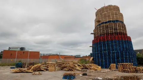 A blue, red and yellow pallets of a bonfire and pallets on the ground. 