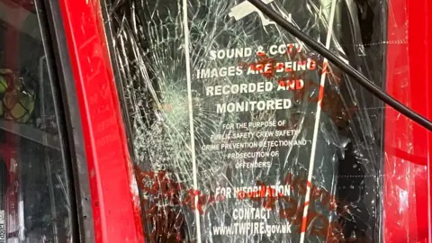 TWFRS A window of a fire engine severly damaged by an item thrown at it. The damaged window is covered in clear cling-film type material. 