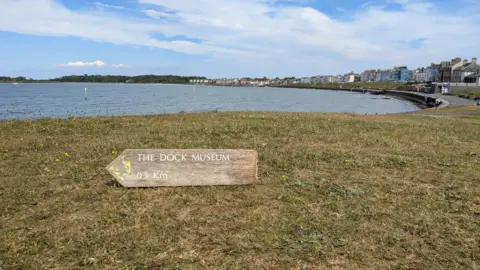Jonny The sign, this time resting on the grass pointing towards the sea.