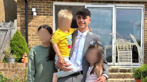 Family handout Brooklyn Bashford, wearing a suit and tie, hugs his younger sisters and lifts his younger brother.
