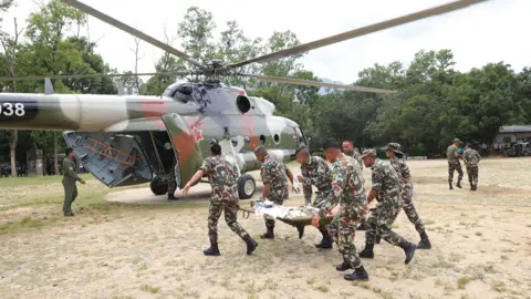 A team of military officers carry a stretcher containing a survivor of the flooding towards a military helicopter in a clearing in Newakot on Wednesday.