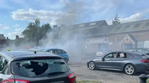  Lizzy Steel / BBC Cars with windows smashed and smoke in the background