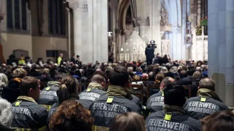 EPA Firefighters, clad in black jackets labeled Magdeburg Fire Department in German, participate in an ecumenical memorial service at Magdeburg Cathedral following the Christmas market incident