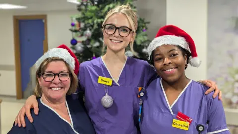 Three women in medical scrub. There is a Christmas tree behind them.