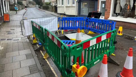 Fencing and cones around the large sinkhole in the middle of the road