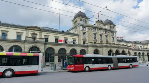 A wide shot of of Winterthur train station taken on a spring day in 2019. Two buses are waiting outside the station.