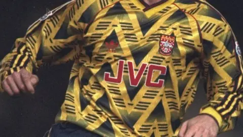 Getty Images An Arsenal player wearing a black and yellow away strip, from the early 1990s, with the old red badge on it.