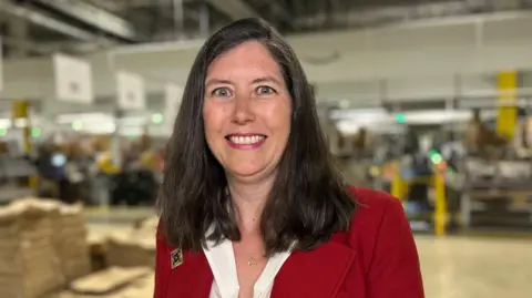 Kate Bradbrook/BBC Clare Bottle, from the UK Warehousing Association, in a red blazer and white shirt. She has brown hair which is just slightly longer than shoulder length.