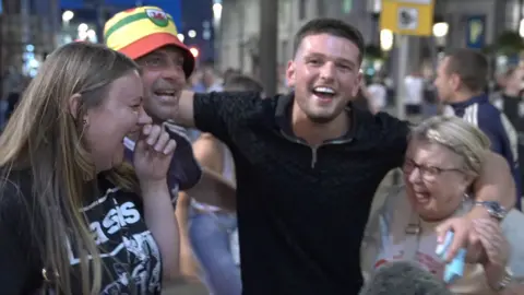 Four Oasis fans cheer in the street.